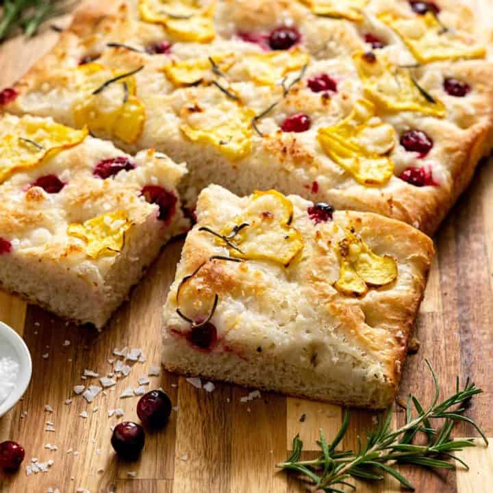 Focaccia topped with squash and cranberries on a wood cutting board