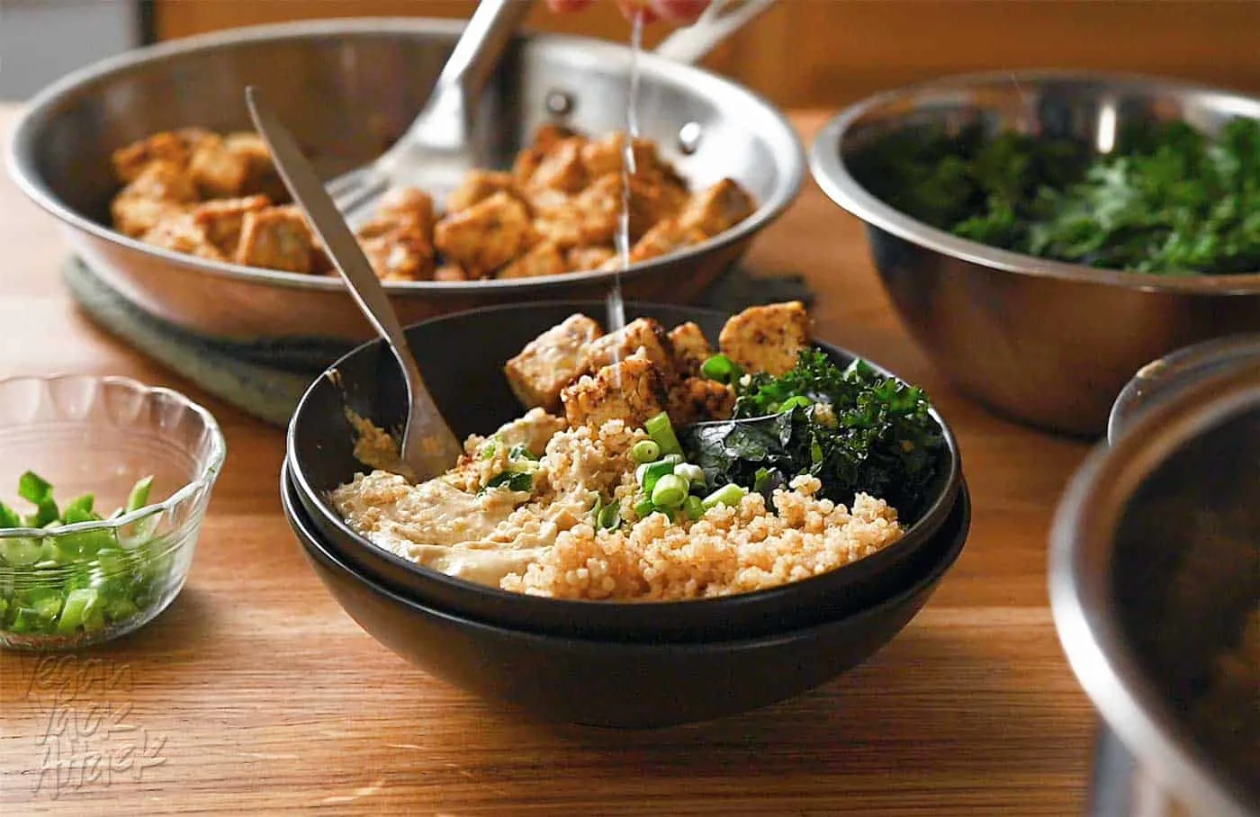 Lemon wedge being squeezed over a bowl with quinoa, kale, tempeh, and spread