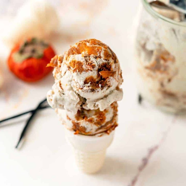 Two scoops of persimmon vanilla ice cream on a cone, next to a persimmon