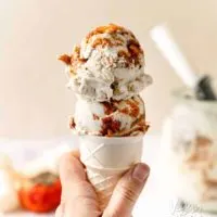 A hand holding Two scoops of persimmon vanilla ice cream on a cone, next to a persimmon