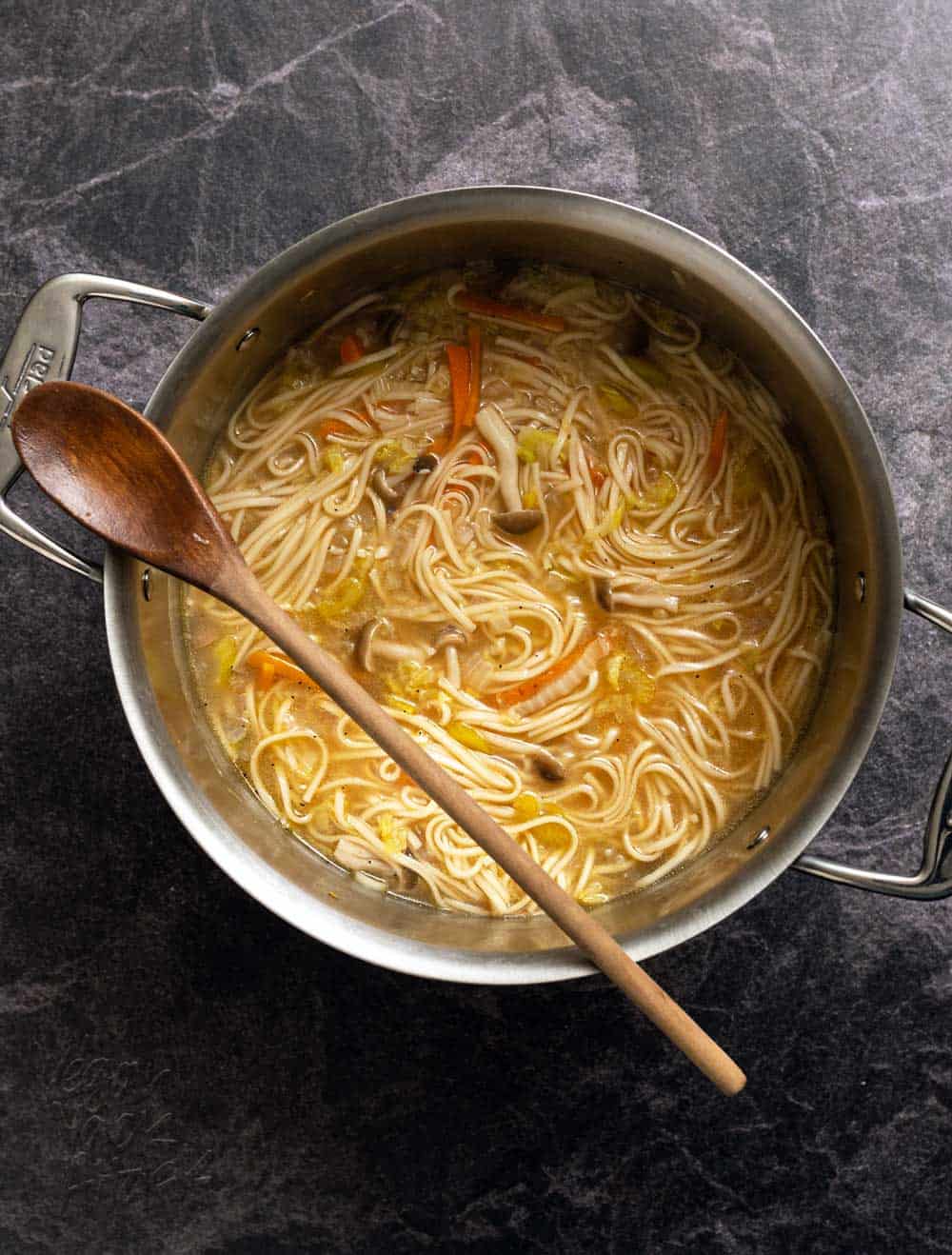 Noodle soup in a large metal pot with wooden spoon