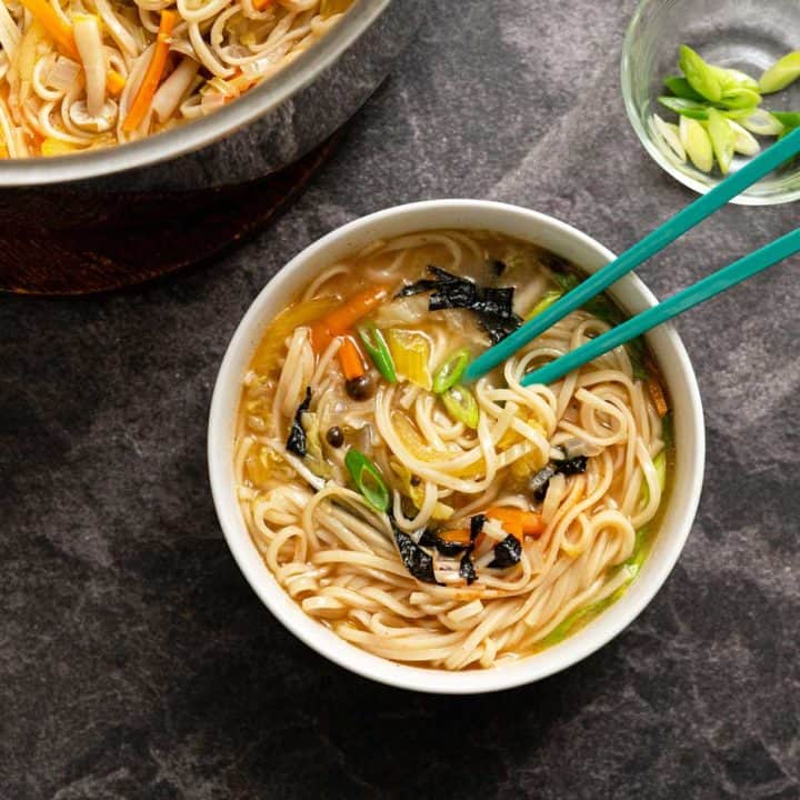 Udon noodle soup in a large white bowl with teal chopsticks