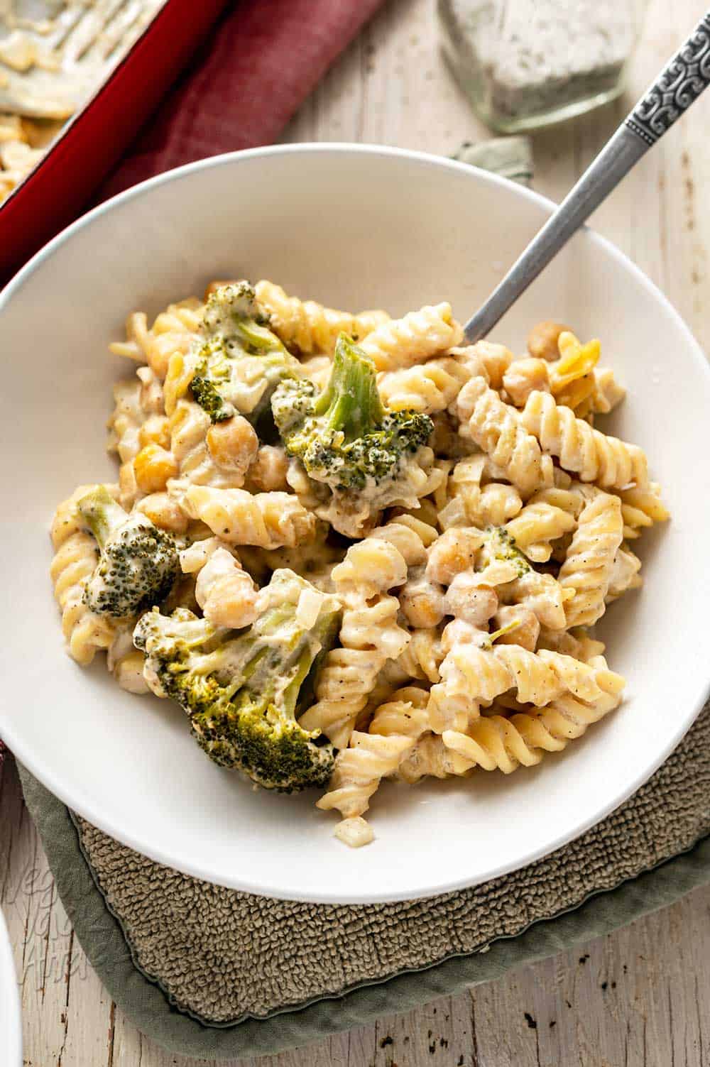 Close up of white bowl with No-Boil Broccoli Pasta Bake next to a casserole dish