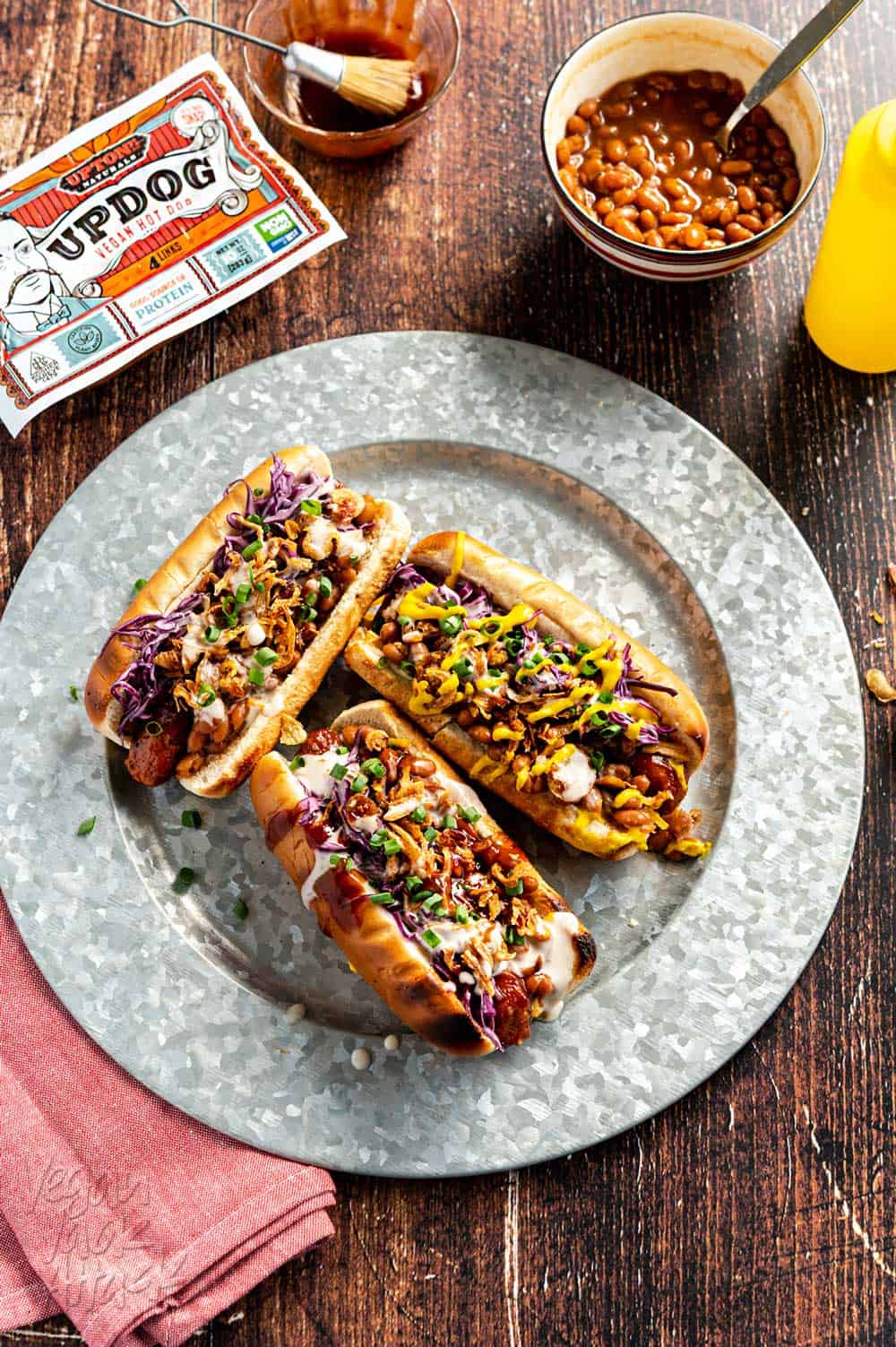 Three loaded vegan hot dogs on a steel plate and wood table