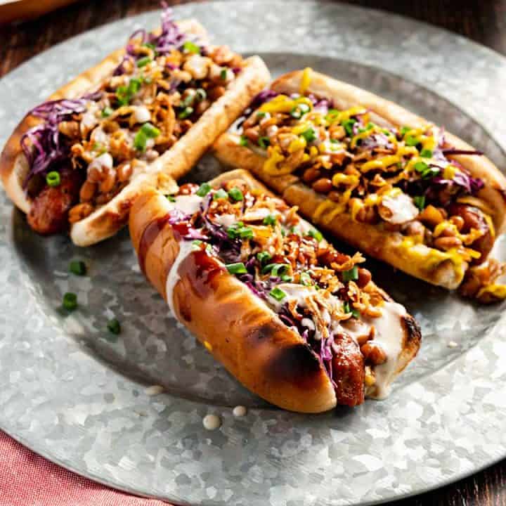 Three loaded vegan hot dogs on a steel plate