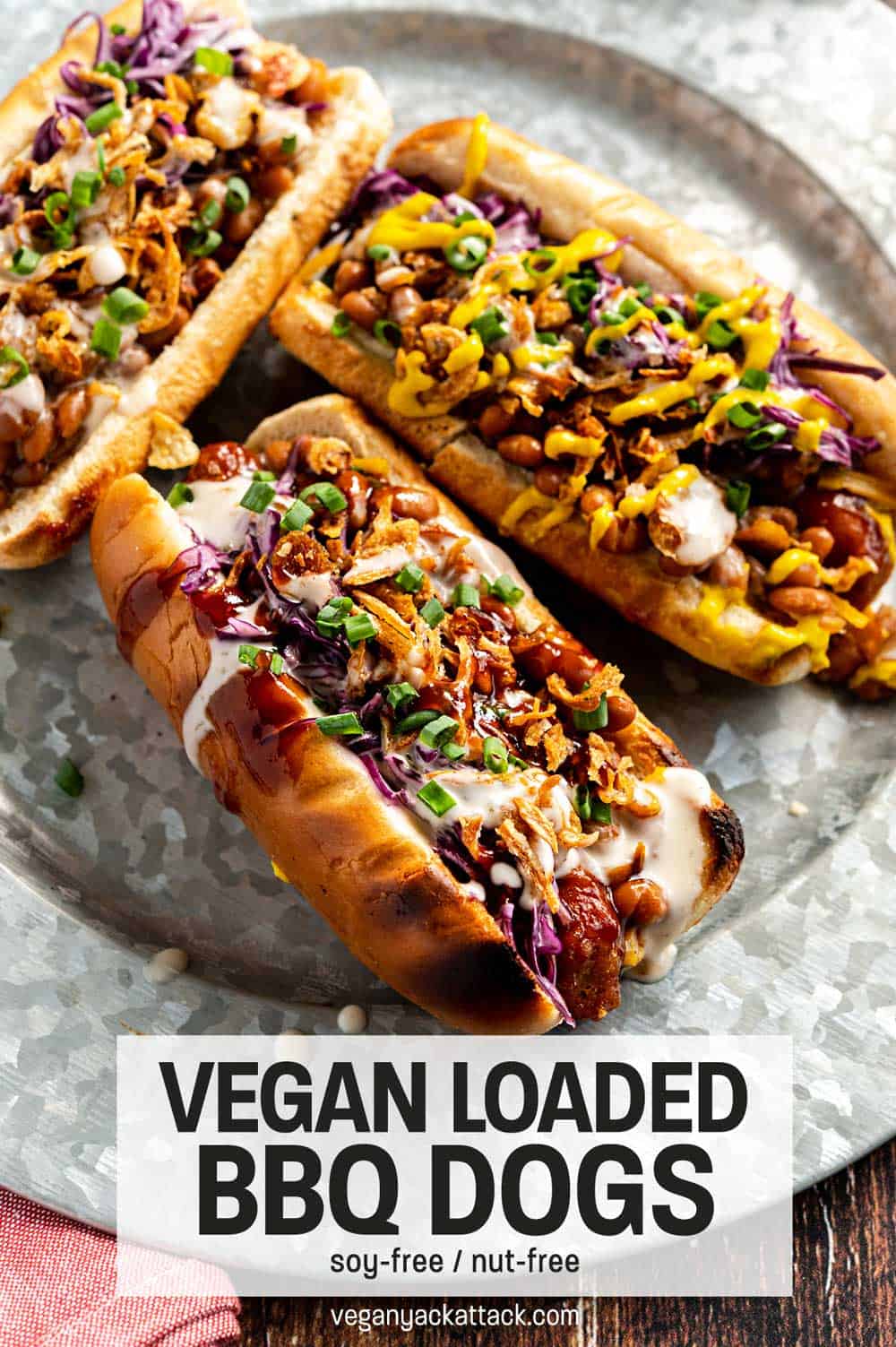 Three loaded vegan hot dogs on a steel plate