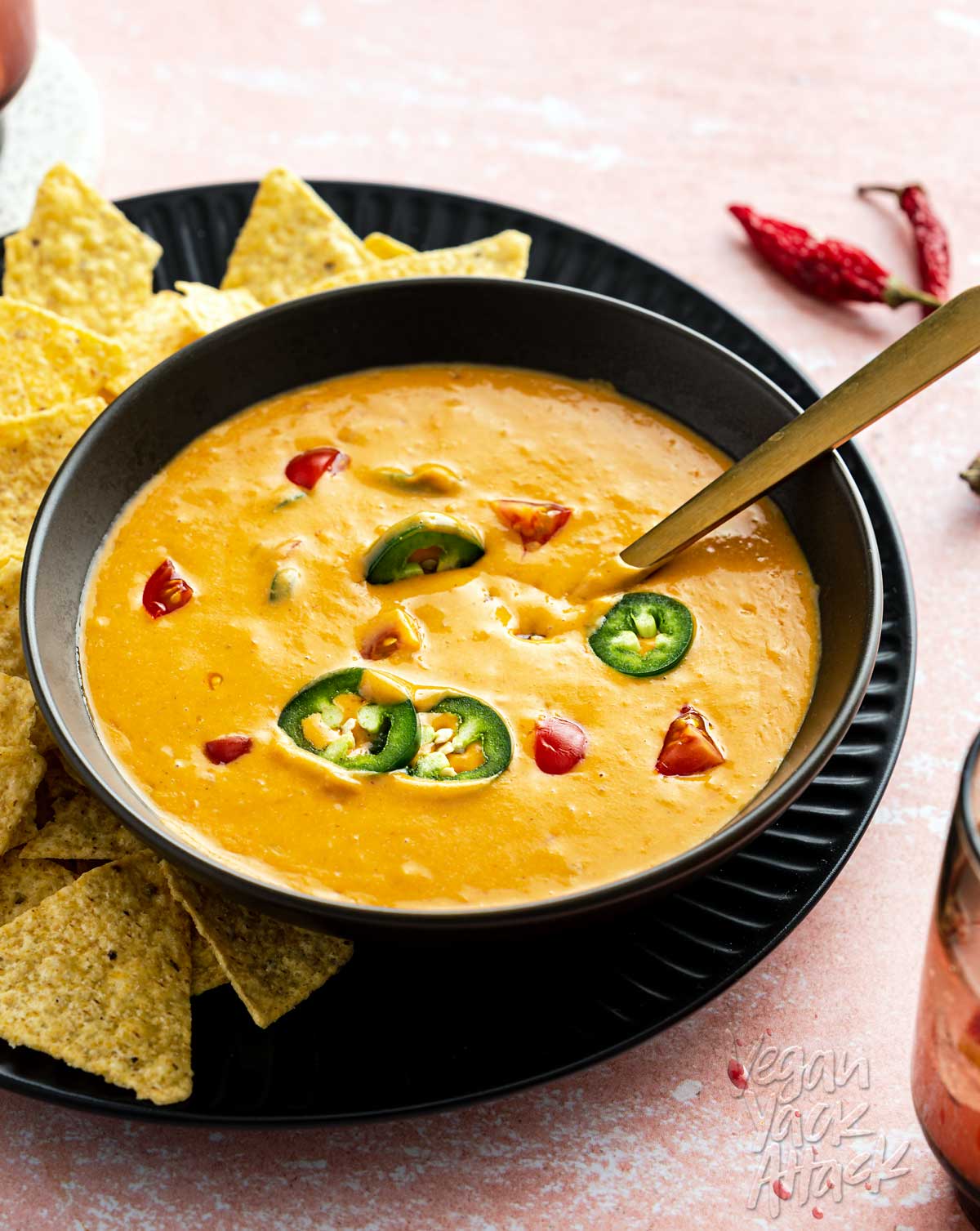 Bowl of bright orange queso dip on a plate with chips, on pink background