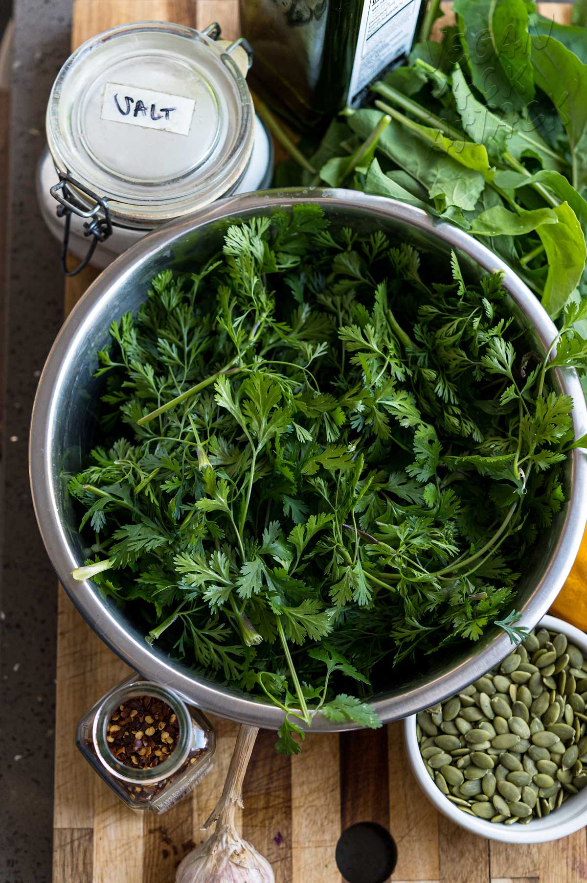 large bowl of cilantro with seeds and salt on a cutting board