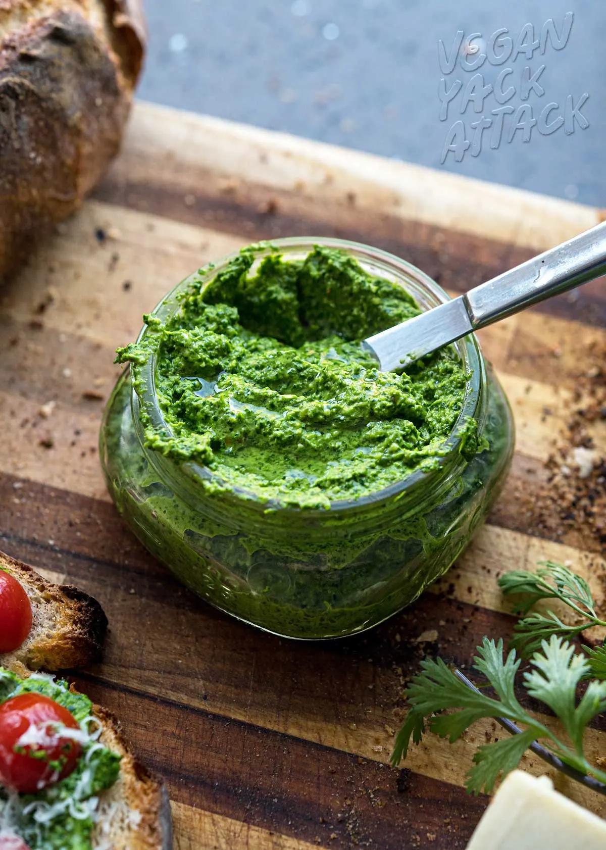 small jar of bright green pesto with knife in it on a cutting board