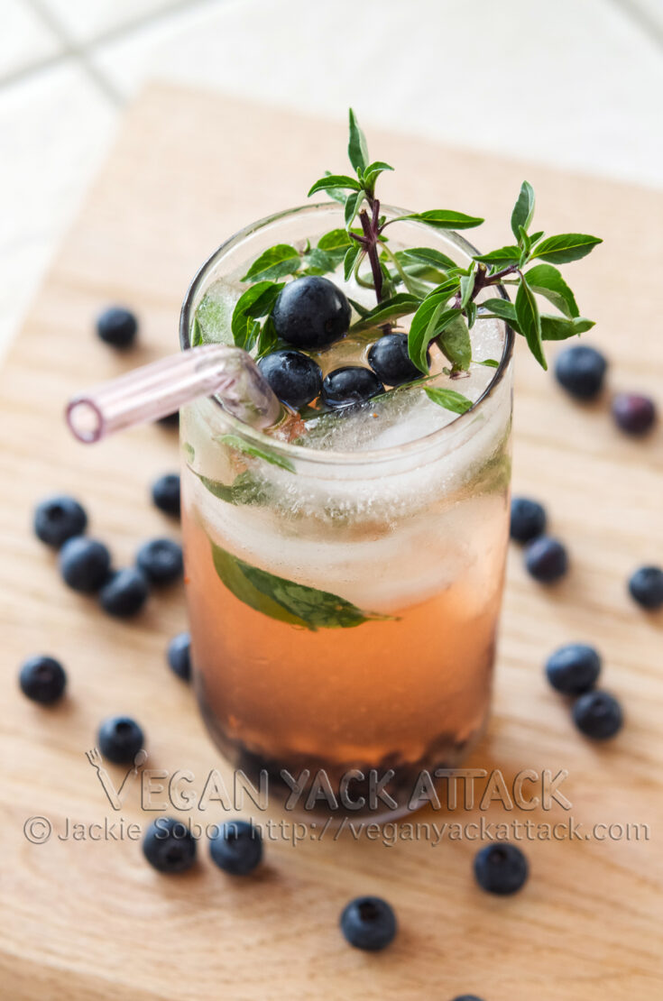 Pink-hued cocktail in a glass with blueberries and Thai basil as garnish