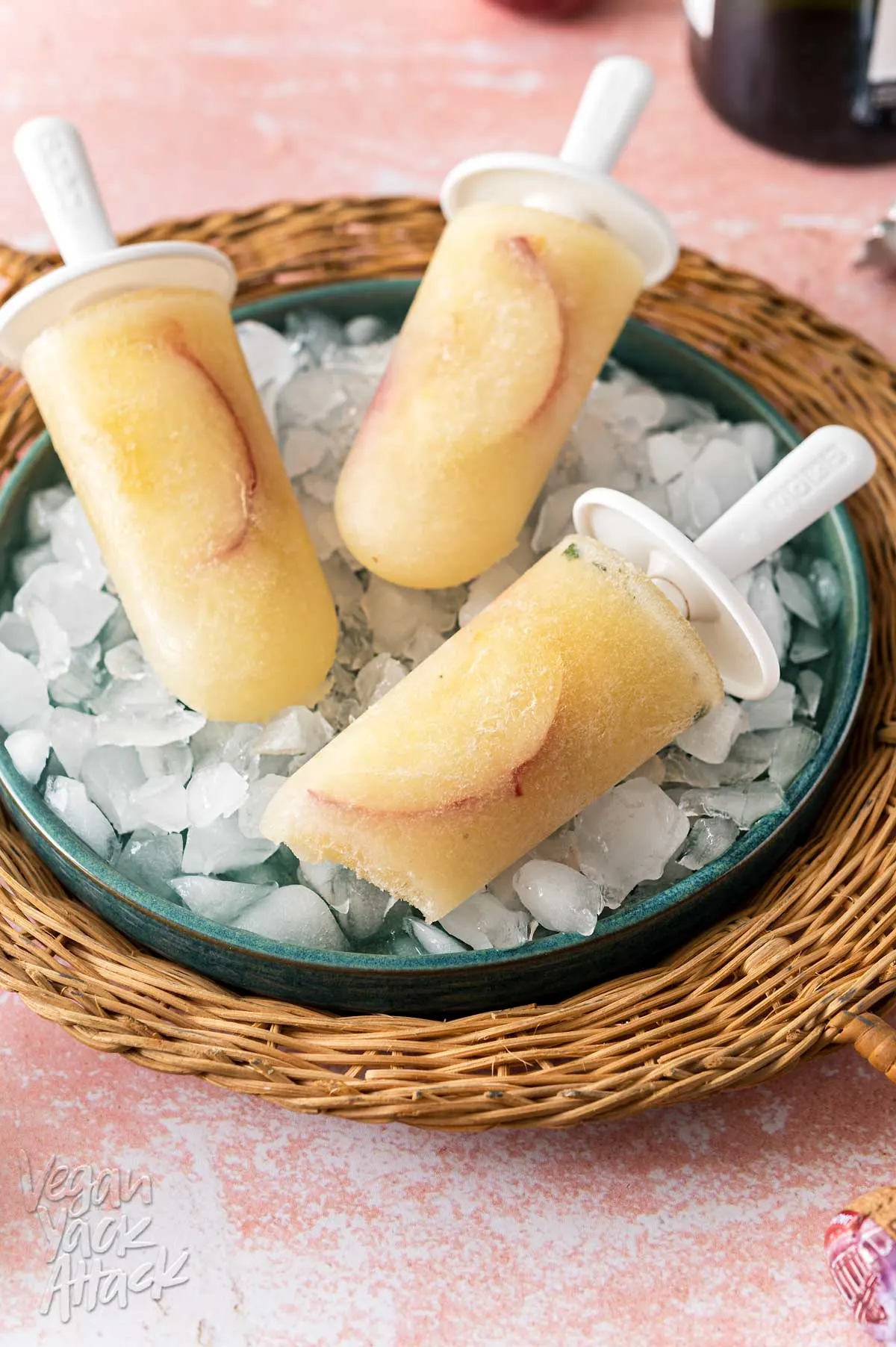 Wicker tray holding three peach Bellini popsicles on a pink table