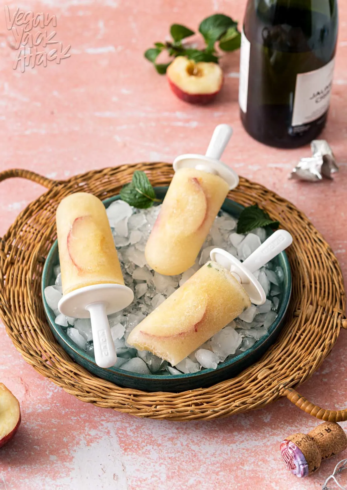 Wicker tray holding three peach Bellini popsicles on a pink table