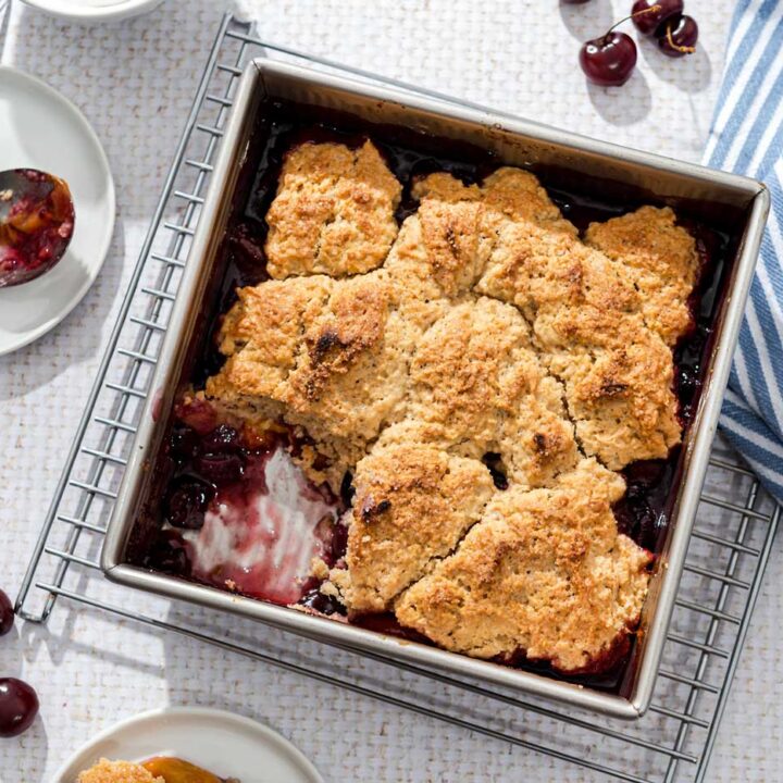 Square baking dish of fruit cobbler on a wire rack, on a white table cloth