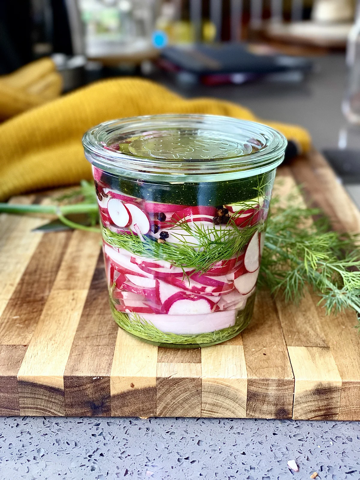 Weck jar with layers of dill and sliced radish, on a cutting board