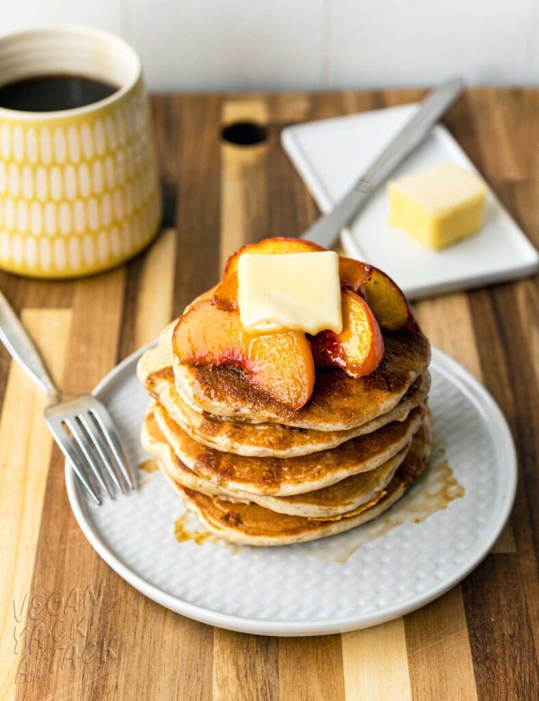 Stack of fluffy pancakes on a plate, topped with peaches