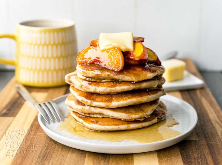 Stack of fluffy pancakes on a plate, topped with peaches