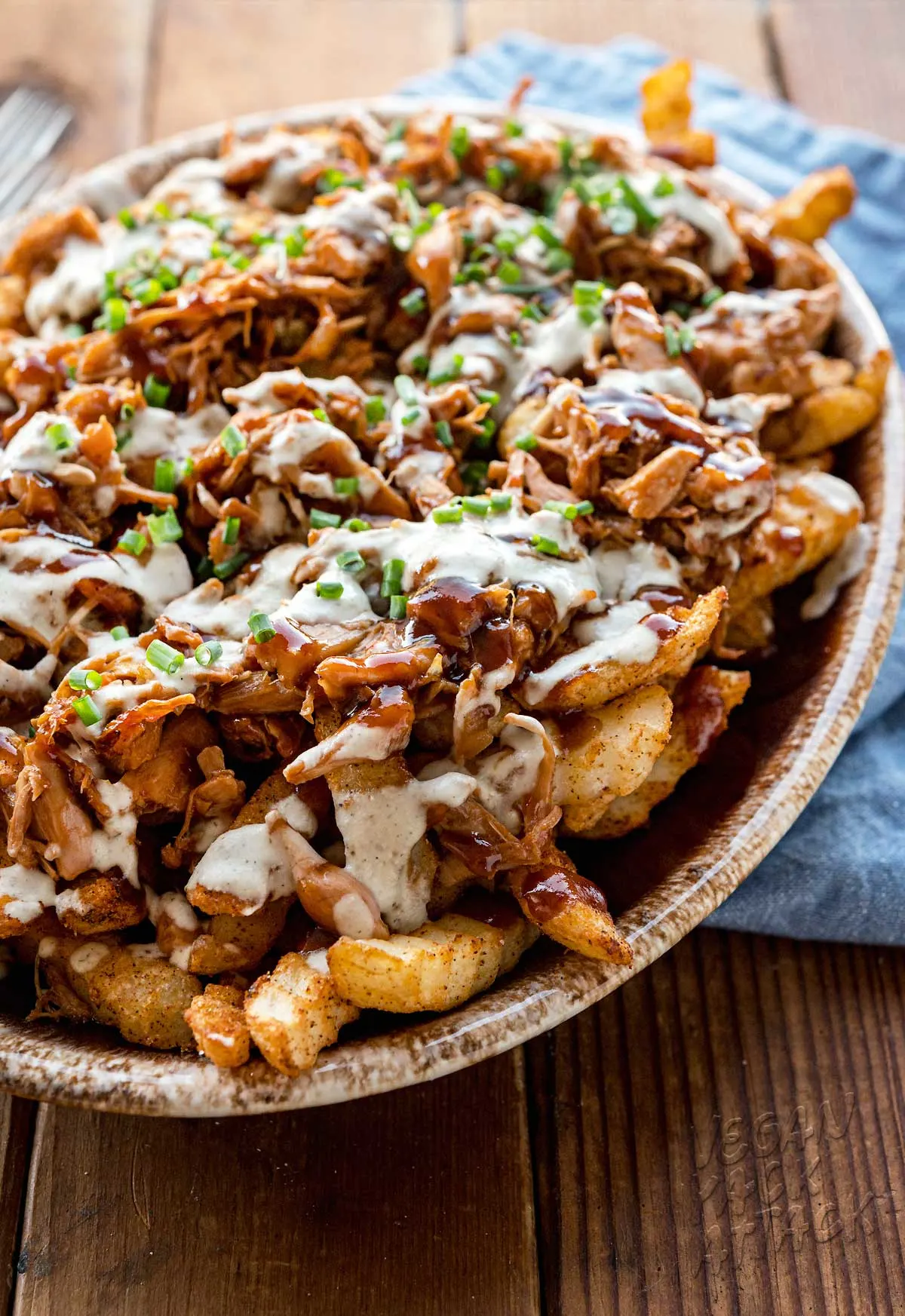 Oval platter with fries topped with jackfruit, sauces, and green onions on a wood table