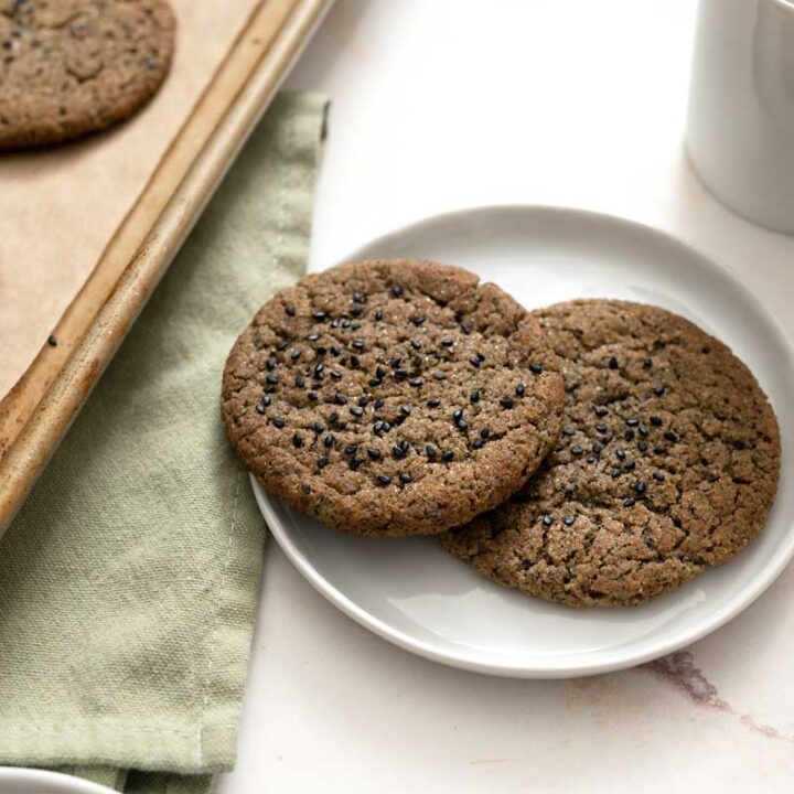 black sesame cookies on plates next to a mug of coffee and baking sheet