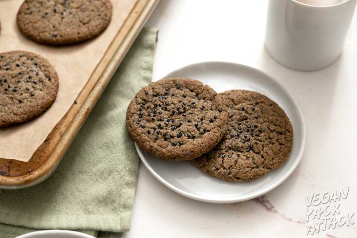 black sesame cookies on plates next to a mug of coffee and baking sheet