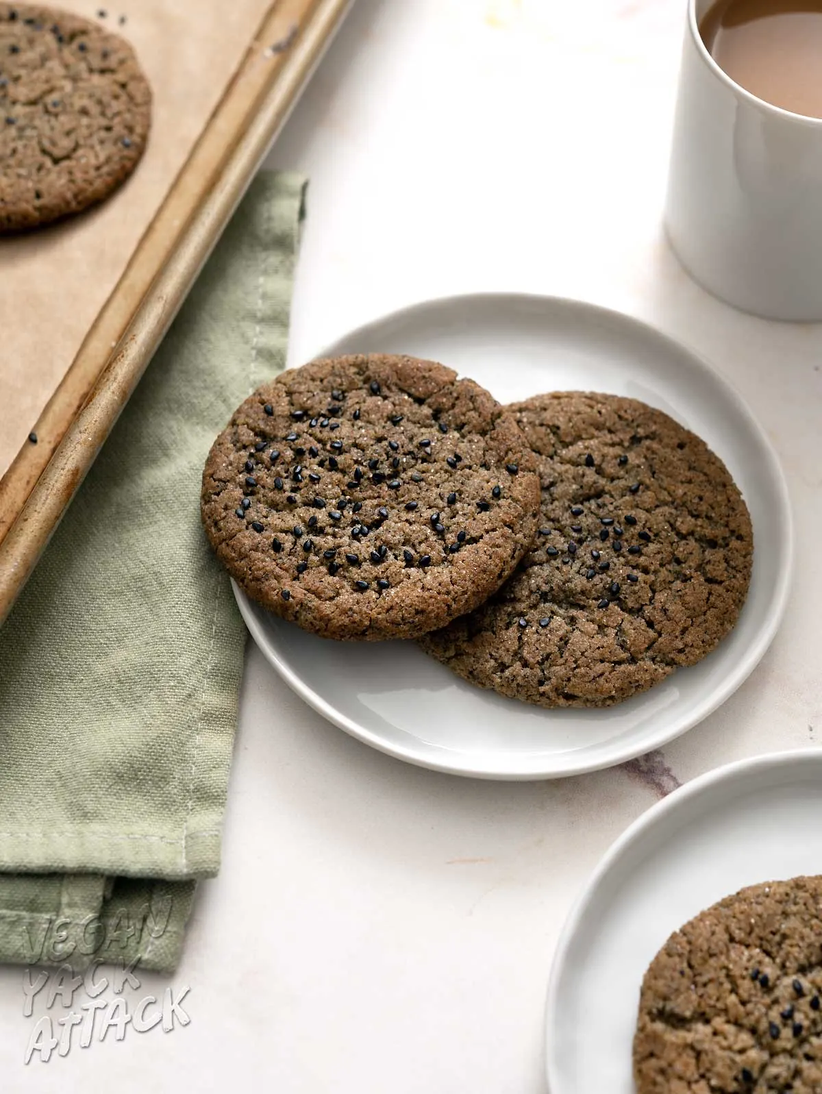 black sesame cookies on plates next to a mug of coffee and baking sheet