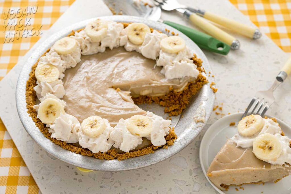 Banana cream pie with slice cut out of it and on a plate next to it with cutlery