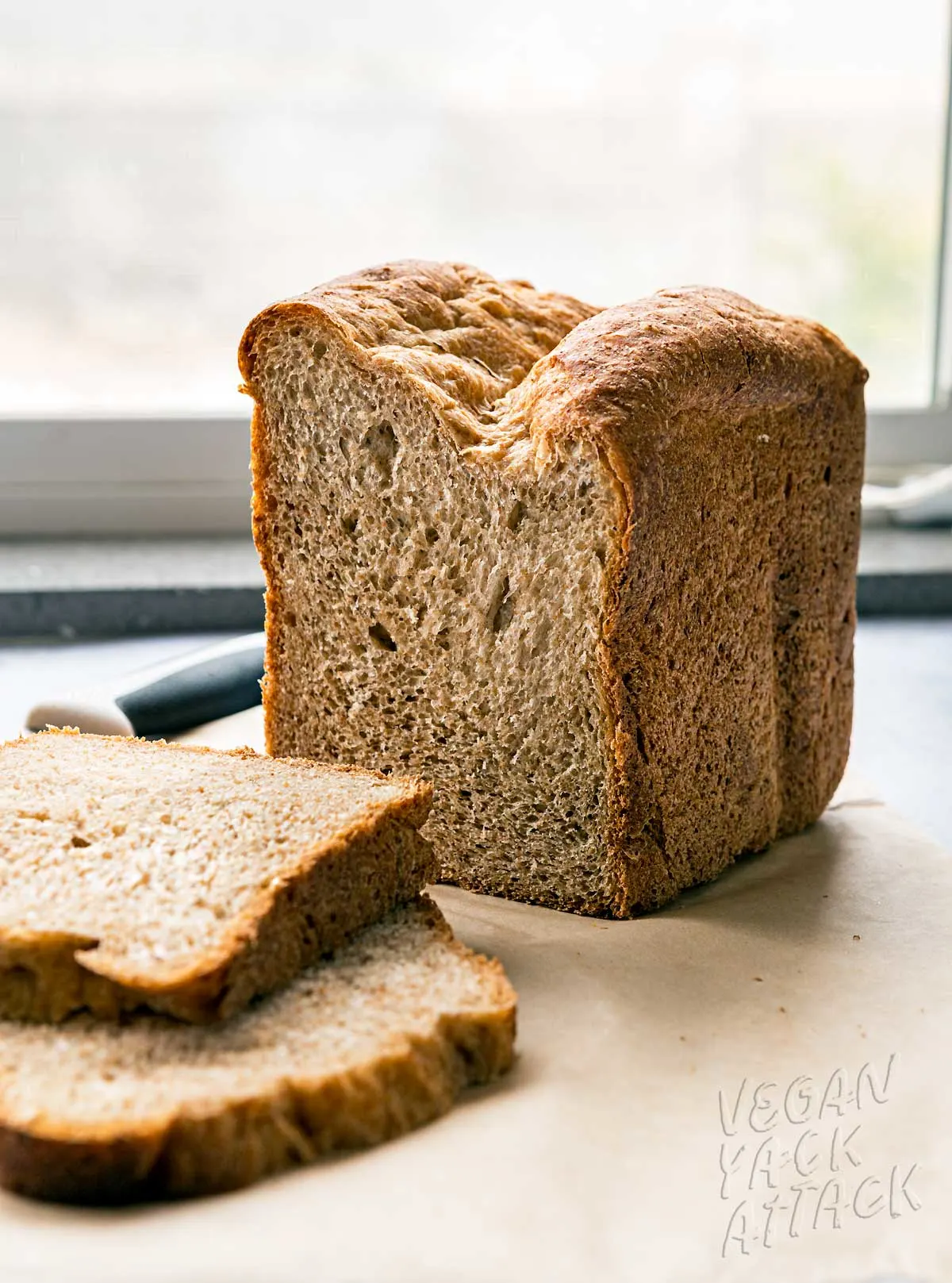 two slices of wheat bread next to the loaf and bread knife