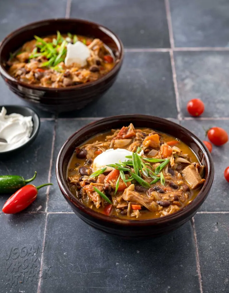 two brown ceramic bowls filled with vegan jackfruit chili on a slate blue tile table