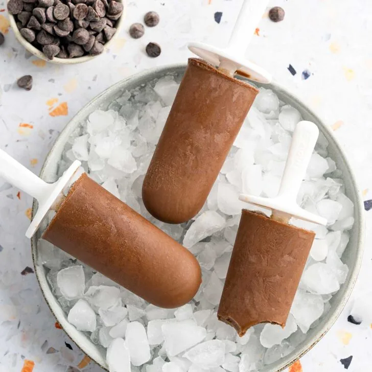 three chocolate popsicles on a plate of crushed ice