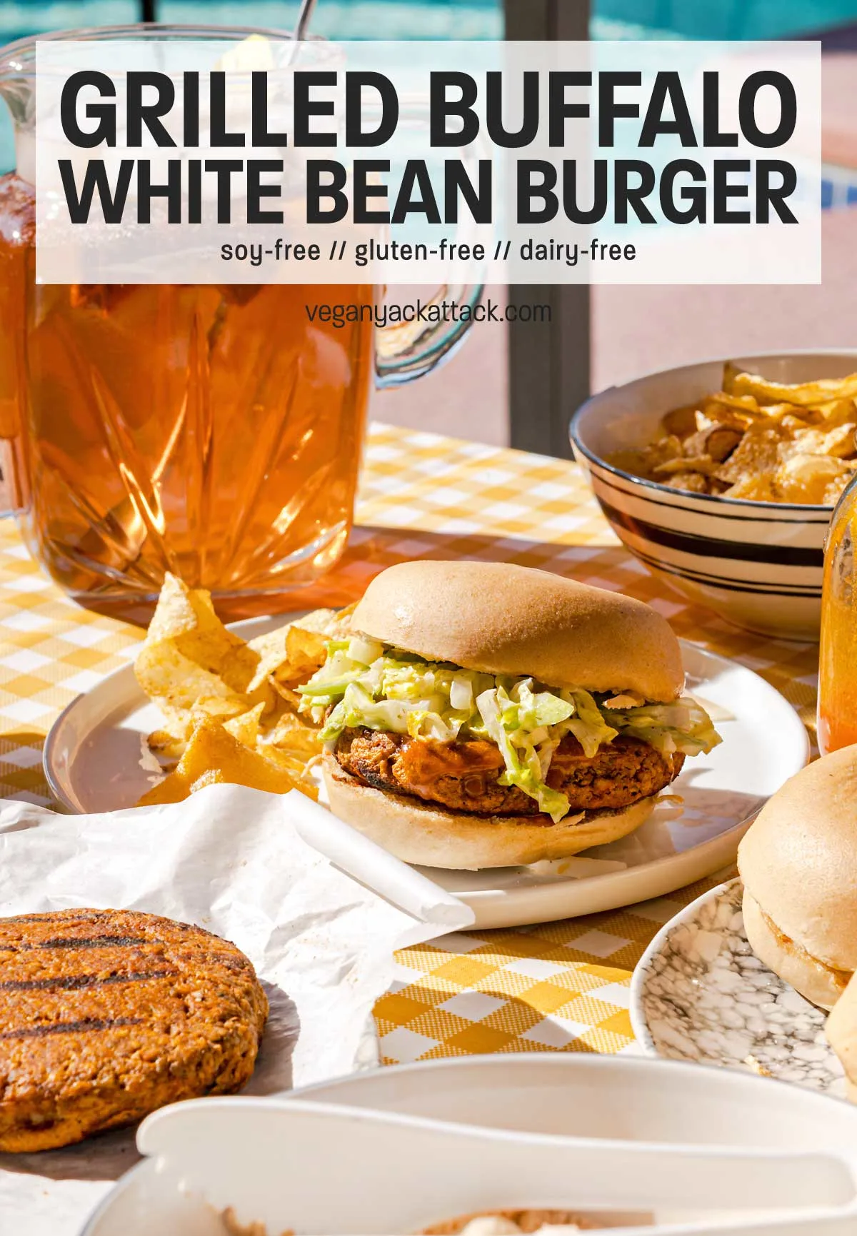 Burger on a plate with chips, in a picnic table setting with pitcher of iced tea