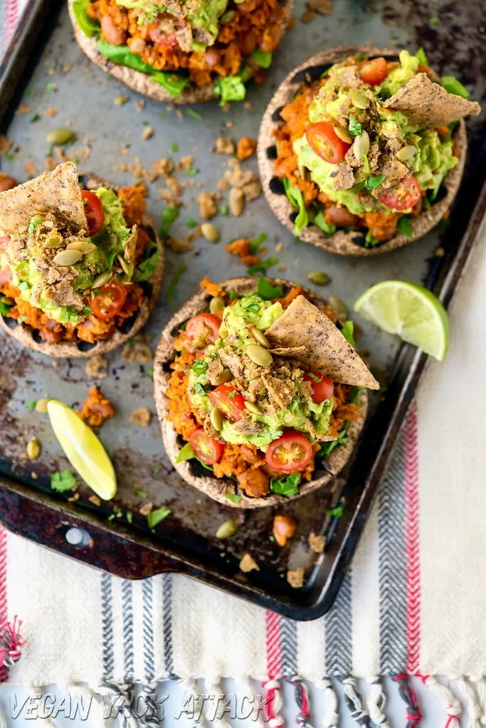 baking sheet with four stuffed mushrooms topped with tomatoes, guacamole and soyrizo