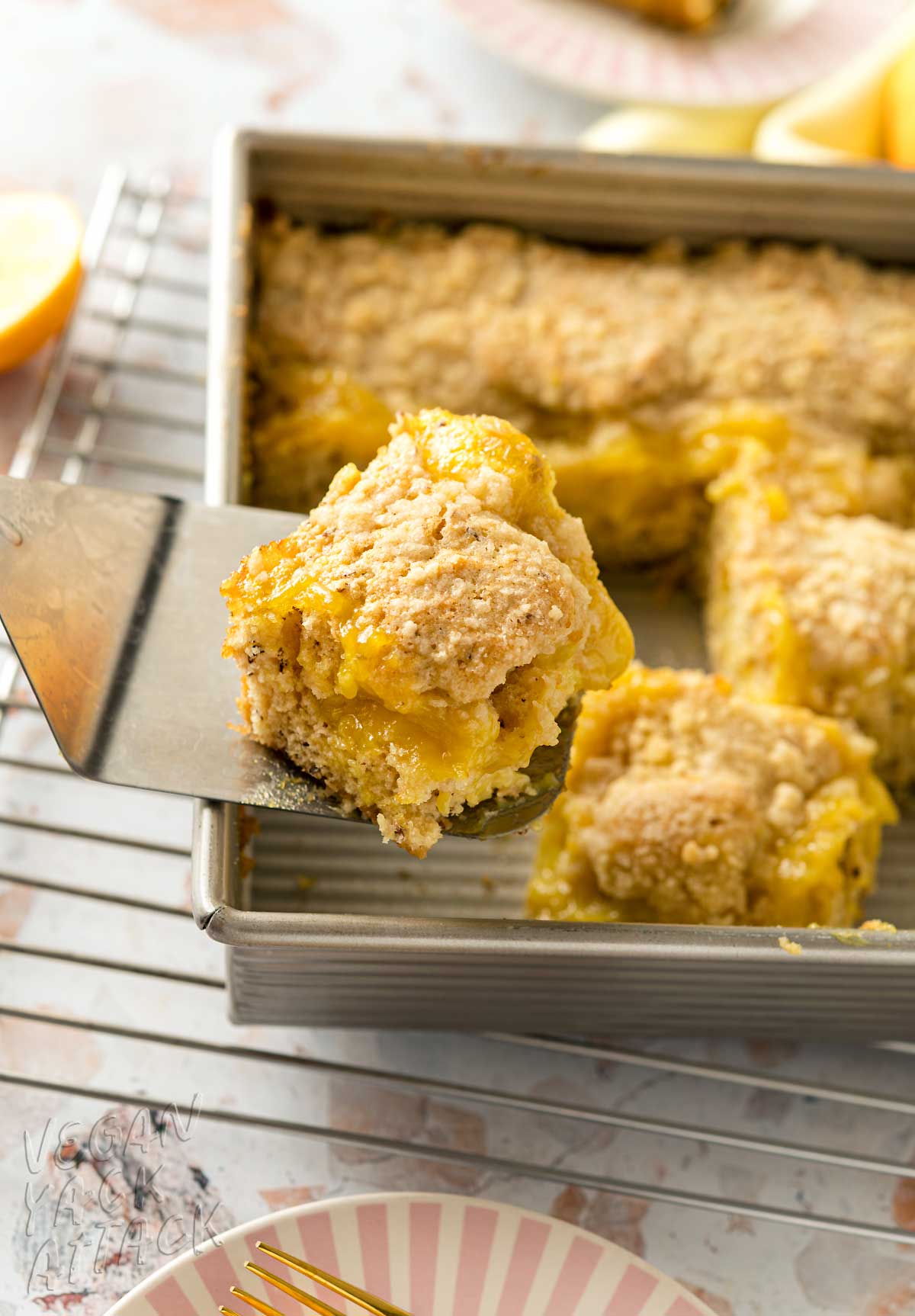 close up of piece of lemon curd coffee cake on a spatula, hovering above a baking dish