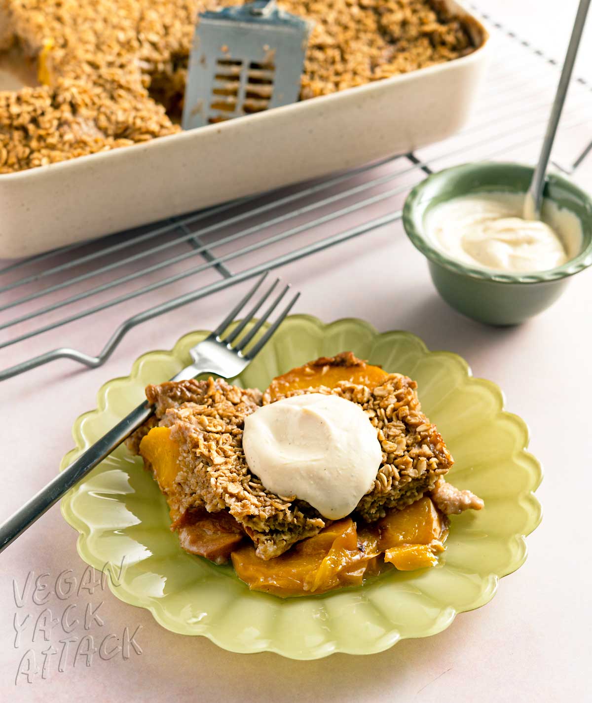 piece of peach cobbler baked oatmeal on a green plate with a small bowl of yogurt